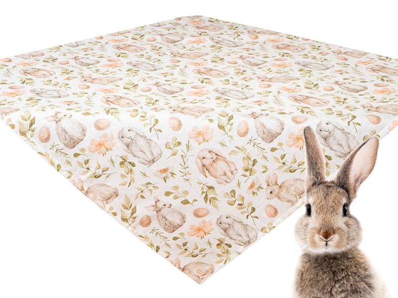Weisse Mitteltischdecke flach liegend bedruckt mit braunen Haeschen, weissen und orangen Blumen und gruenen Zweigen. Davor sitzt ein lebensechter Hase im Bild.