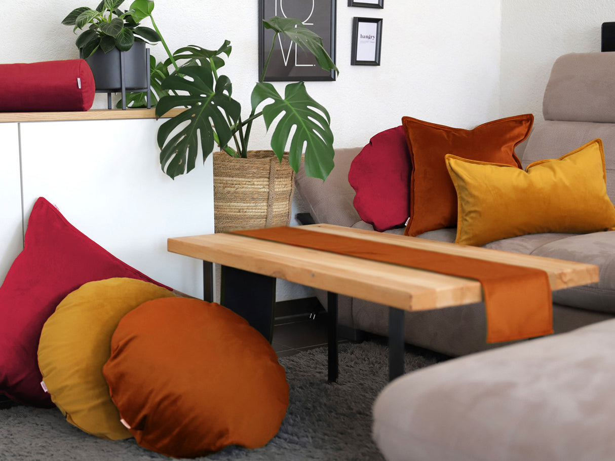 Karmin-rote, rost-orangene und curry-senf-gelbe Samt Kissenbezuege und ein rost-oranges Samt Tischband sind in einem Wohnzimmer dekoriert.