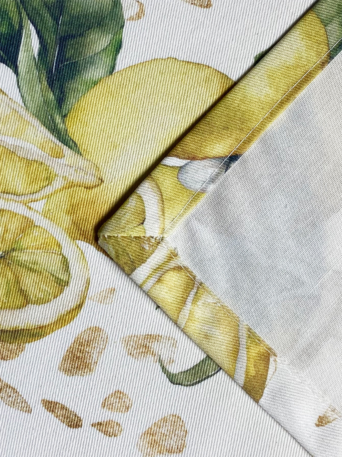 Detailaufnahme einer Ecknaht eines hellbeigen Tischläufers mit Zitronenmuster und goldenen Akzenten.