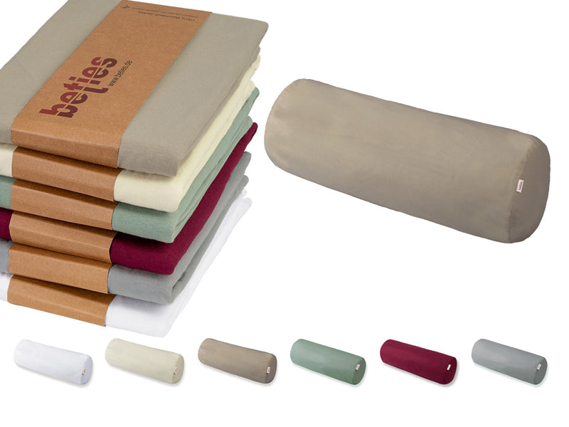 Beige XL-Rolle auf einem weissen Hintergrund. Daneben ein Stapel mit gefalteten Kissenbezuegen in den Uni-Farben Wei�, Hellgrau, Weinrot, Gruen, Natur und Beige.