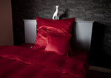Rote Glanz Satin Bettwaesche in einem schwarzen Bett.