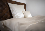 Champagnerfarbene Glanz Satin Bettwaesche in einem braunen Lederbett.