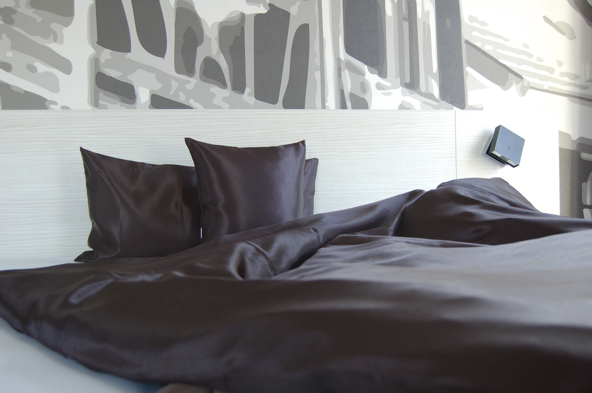 Schwarze Glanz Satin Bettwaesche, dekoriert in einem weissen Holzbett.