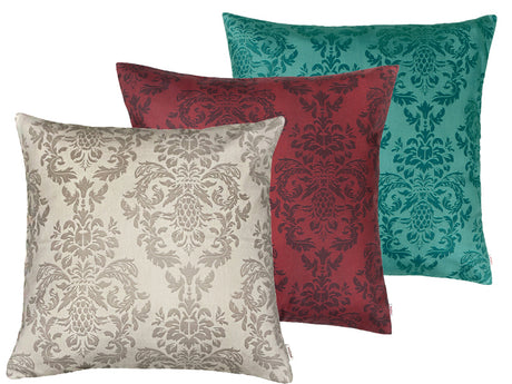 Drei quadratische Kissen hintereinander, bezogen mit Kissenbezuegen in den Farben Beige, Rot und Petrol. Bedruckt sind die Bezuege mit barocken Ornamenten in der jeweiligen Farbe, nur etwas dunkler.