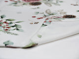 Detailansicht der Kuvertecke einer weissen Tischdecke – Winterdeko mit gefrosteten Rosen in mauve, Kieferzapfen, Beeren und Zweigen – 100% Baumwolle – aus der beties Magie des Winters "Frost-Rose" Kollektion.