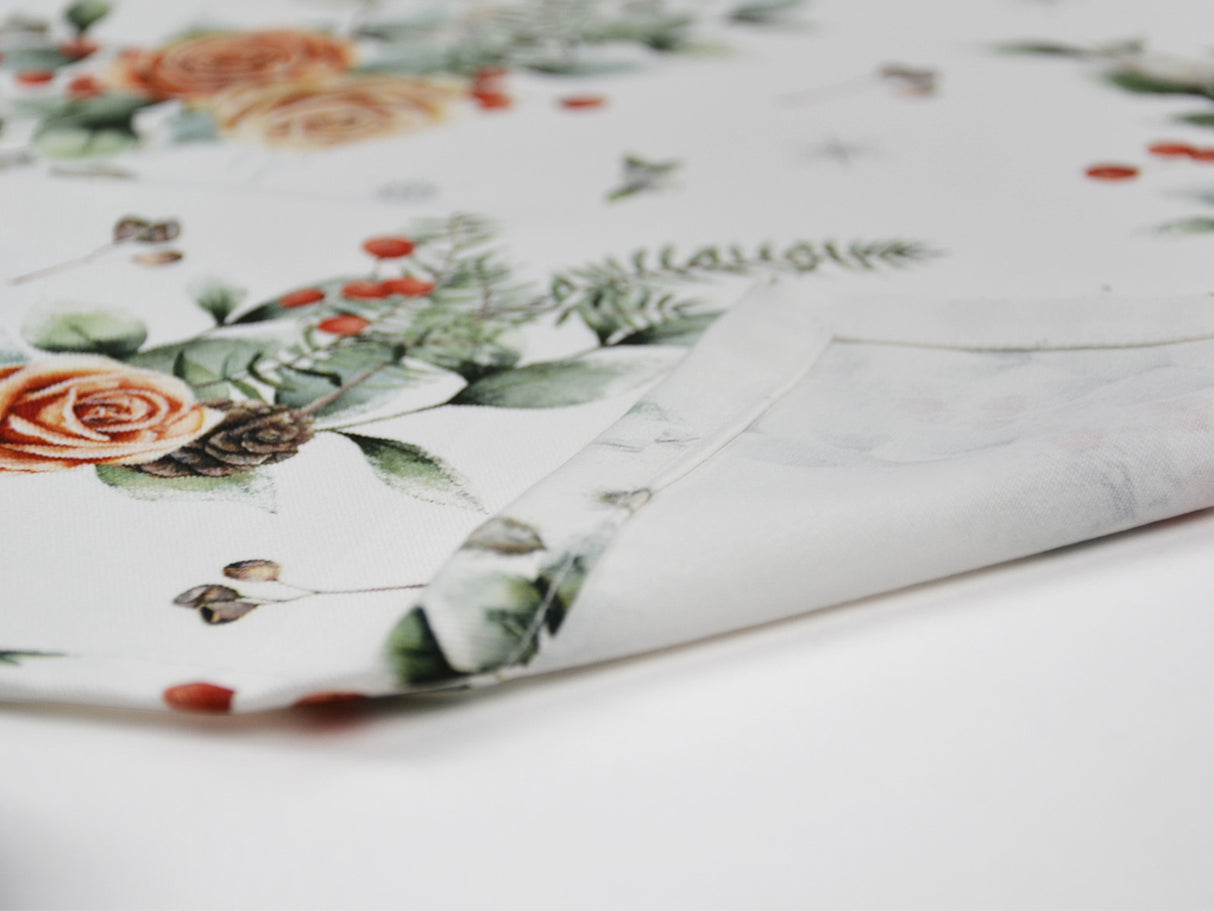 Detailansicht der Kuvertecke einer weissen Tischdecke – Winterdeko mit gefrosteten Rosen in orange, Kieferzapfen, Beeren und Zweigen – 100% Baumwolle – aus der beties Magie des Winters "Frost-Rose" Kollektion.